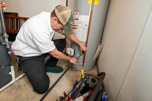 Brothers plumber servicing a residential water heater with tools and safety gear in a utility room.